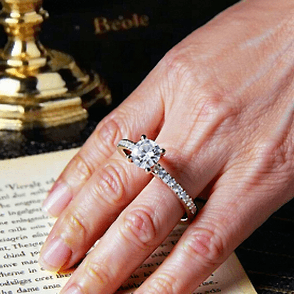 "Create a vintage-themed Instagram ad illustrating the sentimental voyage of an engagement ring, from its velvet-box unveiling under the golden gleam of a desk lamp, to its final moment of gentle placement on a lady's hand. Kick off with a close-up view of the ring that underscores its complex jewel patterns and the metal's gentle shimmer. Use smooth, understated panning shots to transition between elements, deepening the nostalgic atmosphere with a faint sepia tone. The sequence should then shift to intertwined hands